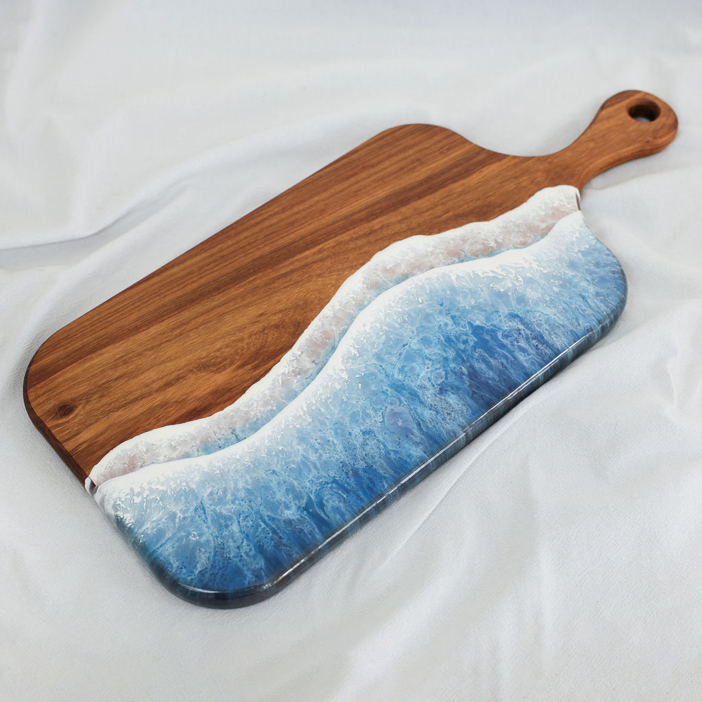 Angled view of handcrafted kiaat wood large paddle serving board with blue ocean resin wave design