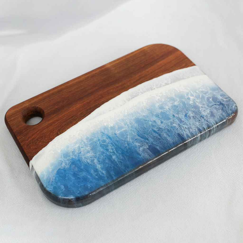 Angled view of handcrafted kiaat wood medium rectangle serving board with blue ocean resin wave design