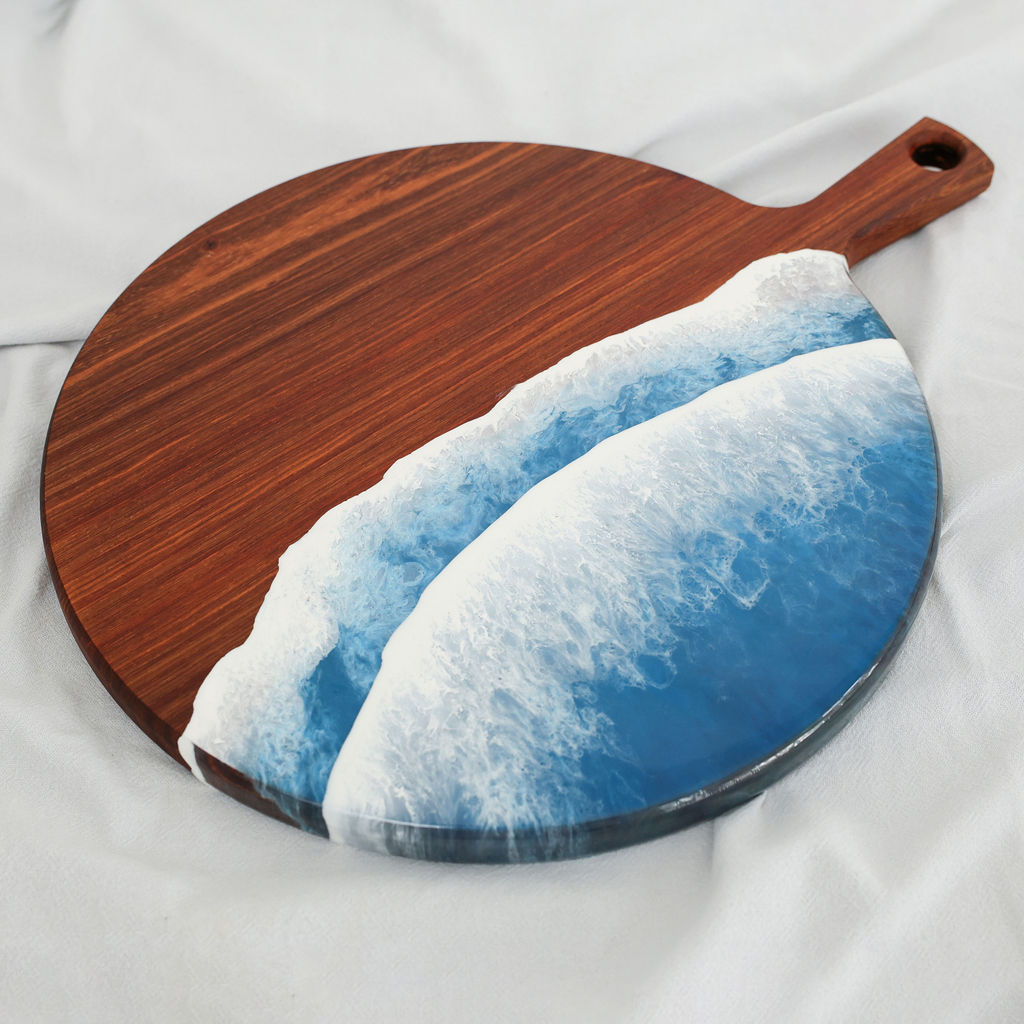 Angled view of handcrafted kiaat wood round serving board with blue ocean resin wave design