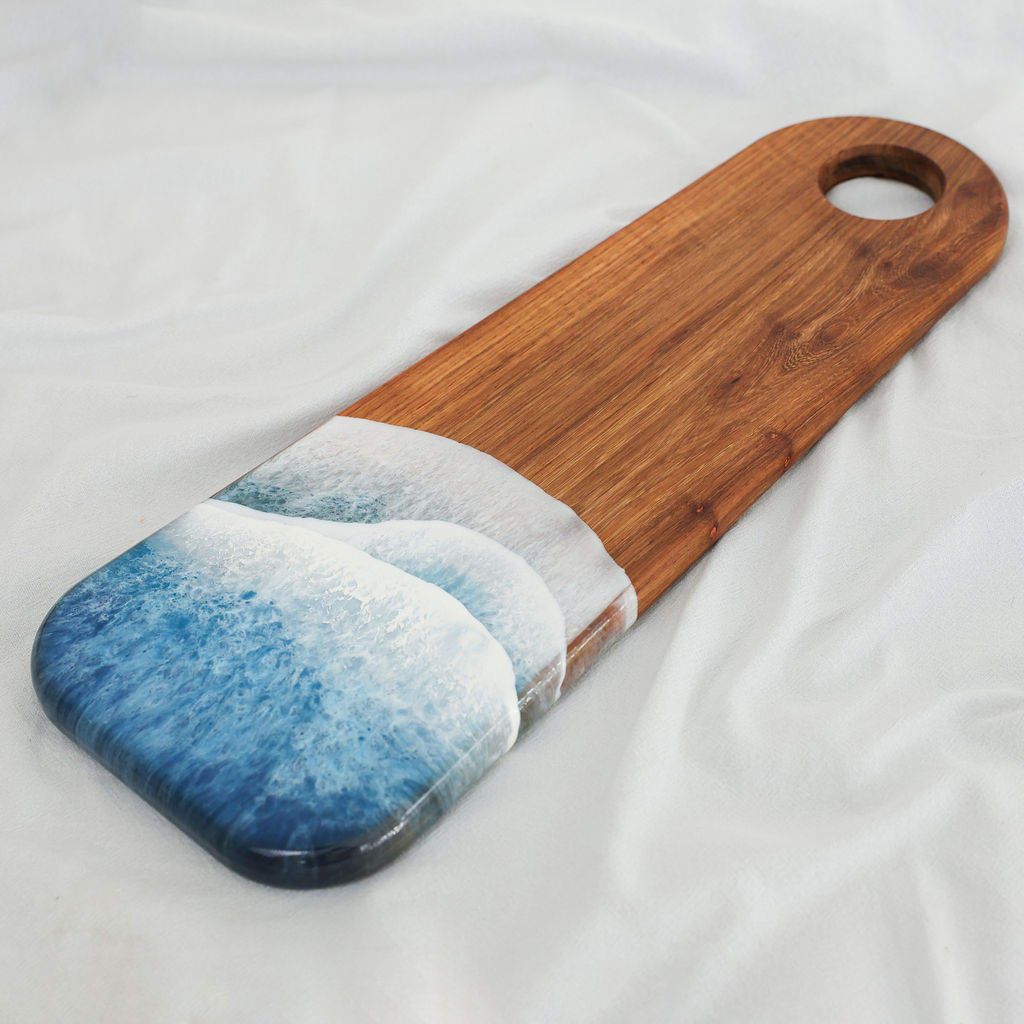 Angled view of handcrafted kiaat wood long serving board with blue ocean resin wave design