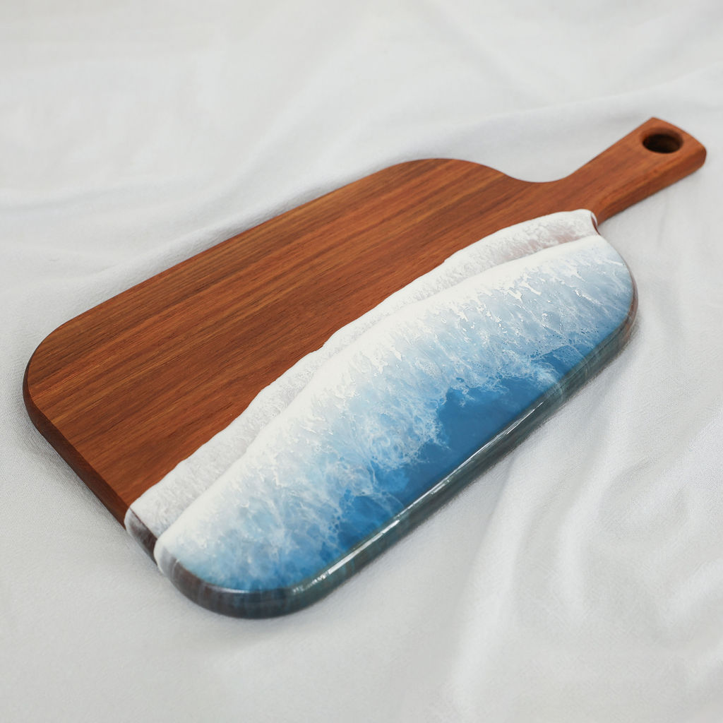 Angled view of handcrafted organic medium paddle serving board made from kiaat wood with blue ocean resin wave design