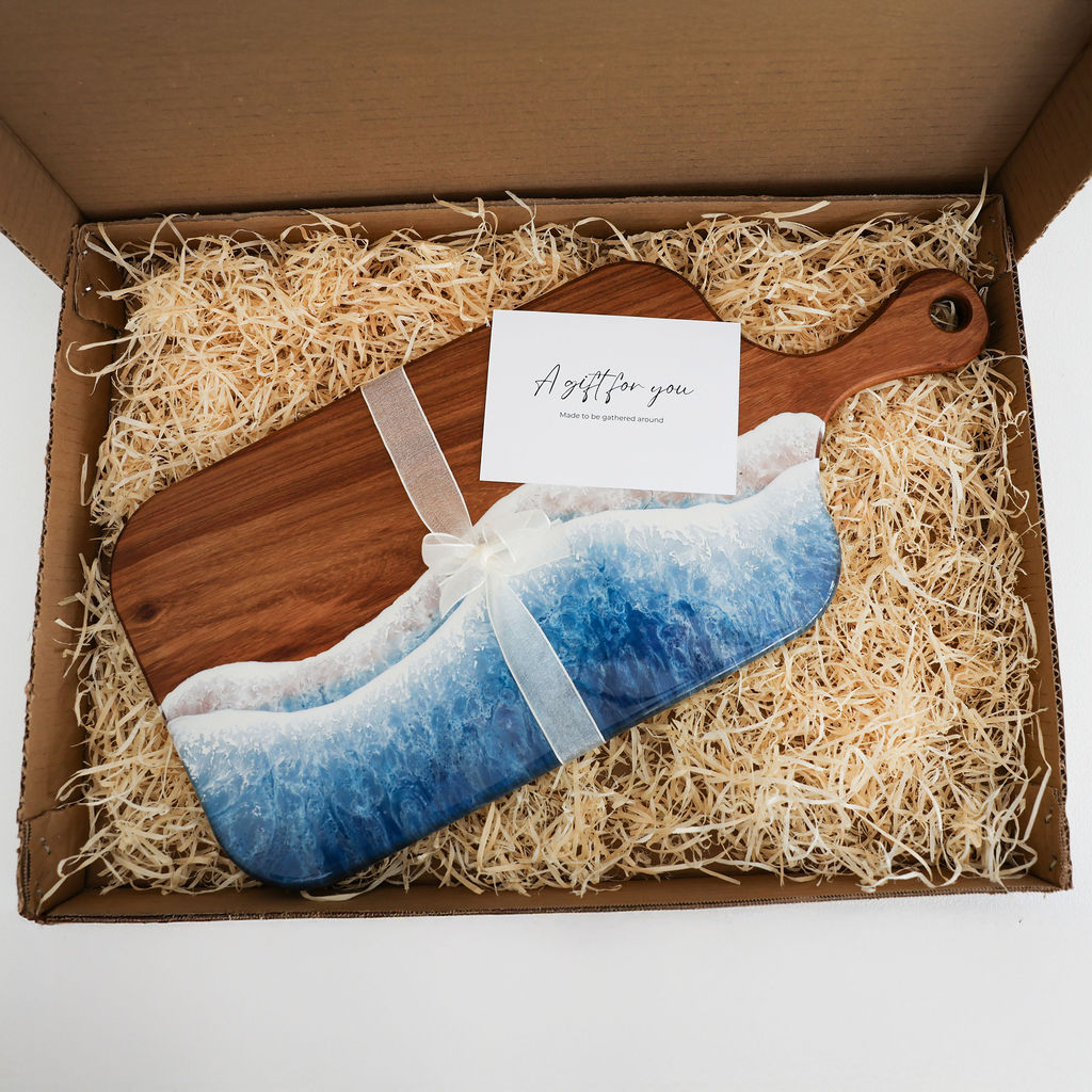 Handcrafted large paddle serving board with ocean resin wave design packaged in a gift box with ribbon and gift tag