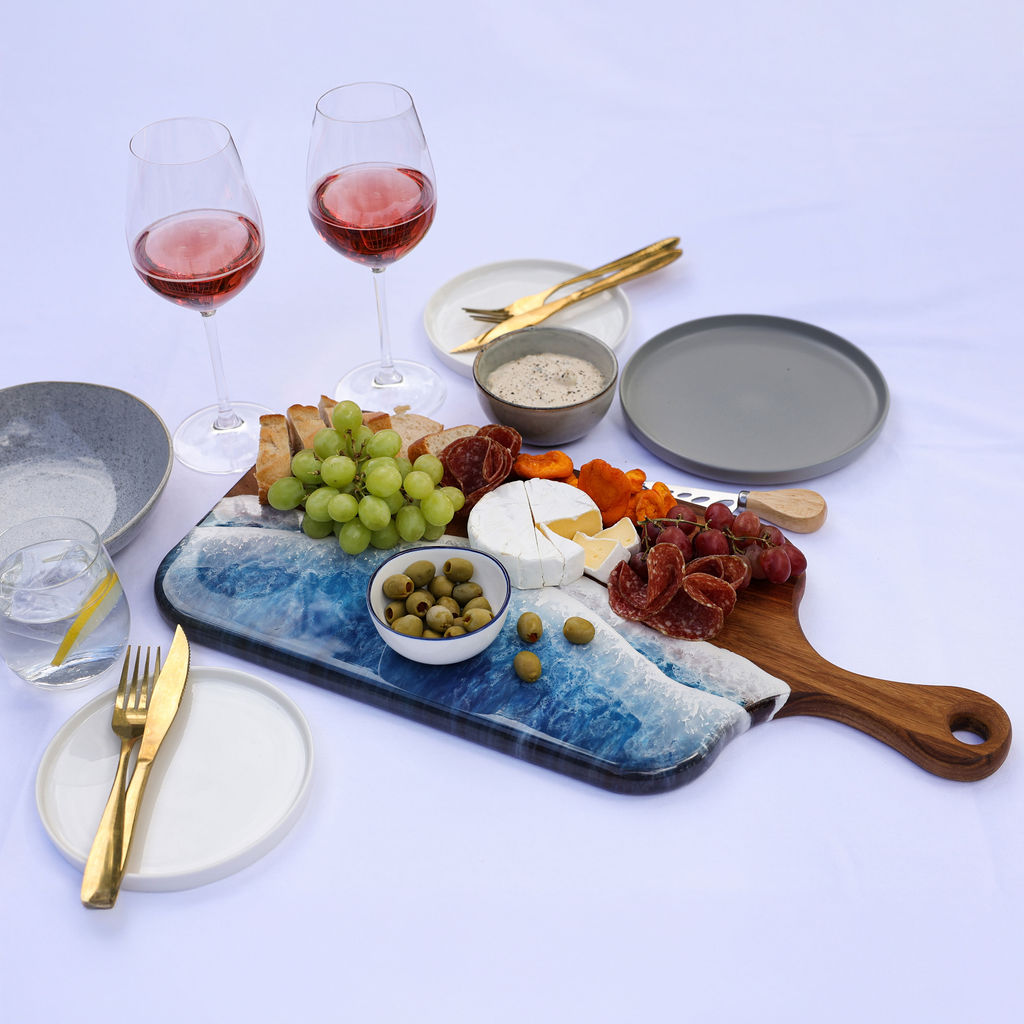 Handcrafted large paddle serving board with ocean resin wave design styled with a variety of foods for entertaining