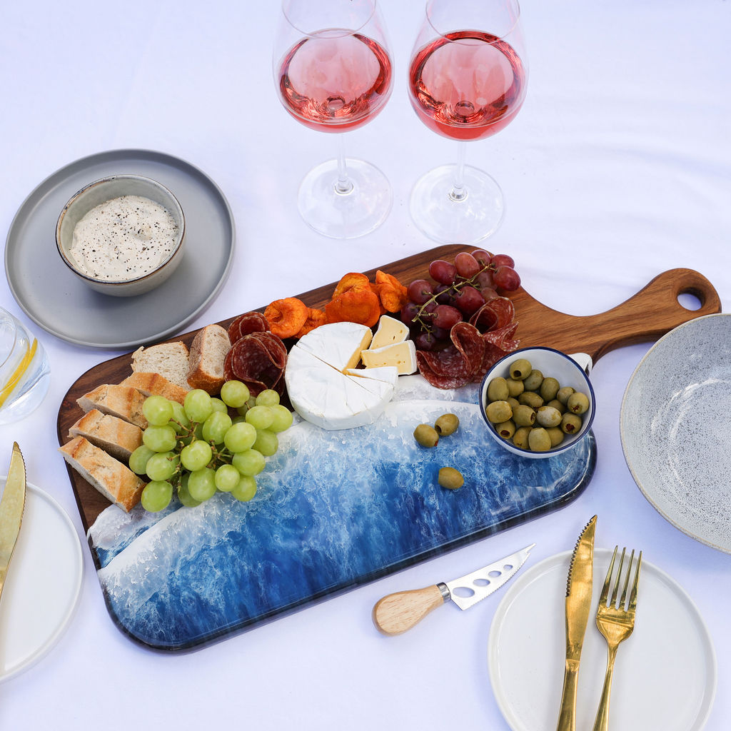 Handcrafted large paddle serving board with ocean resin wave design styled with a variety of foods for entertaining