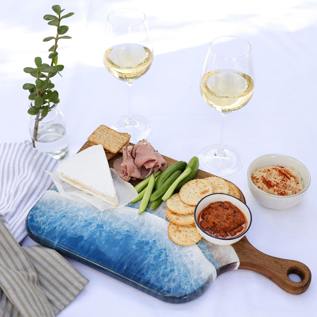 Handcrafted medium paddle serving board with ocean resin wave design styled with a variety of foods for entertaining