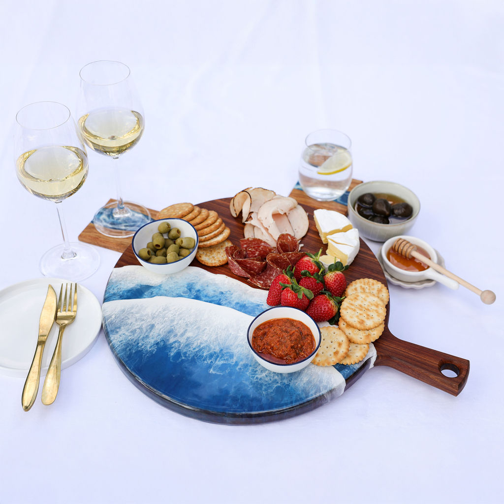 Handcrafted round paddle serving board with ocean resin design styled with a variety of foods for hosting and entertaining