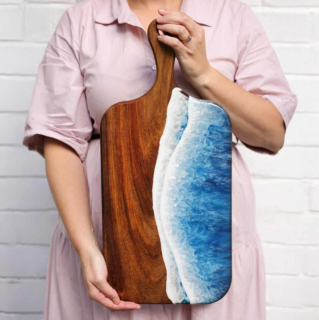 Founder holding a large paddle serving board with ocean resin wave design