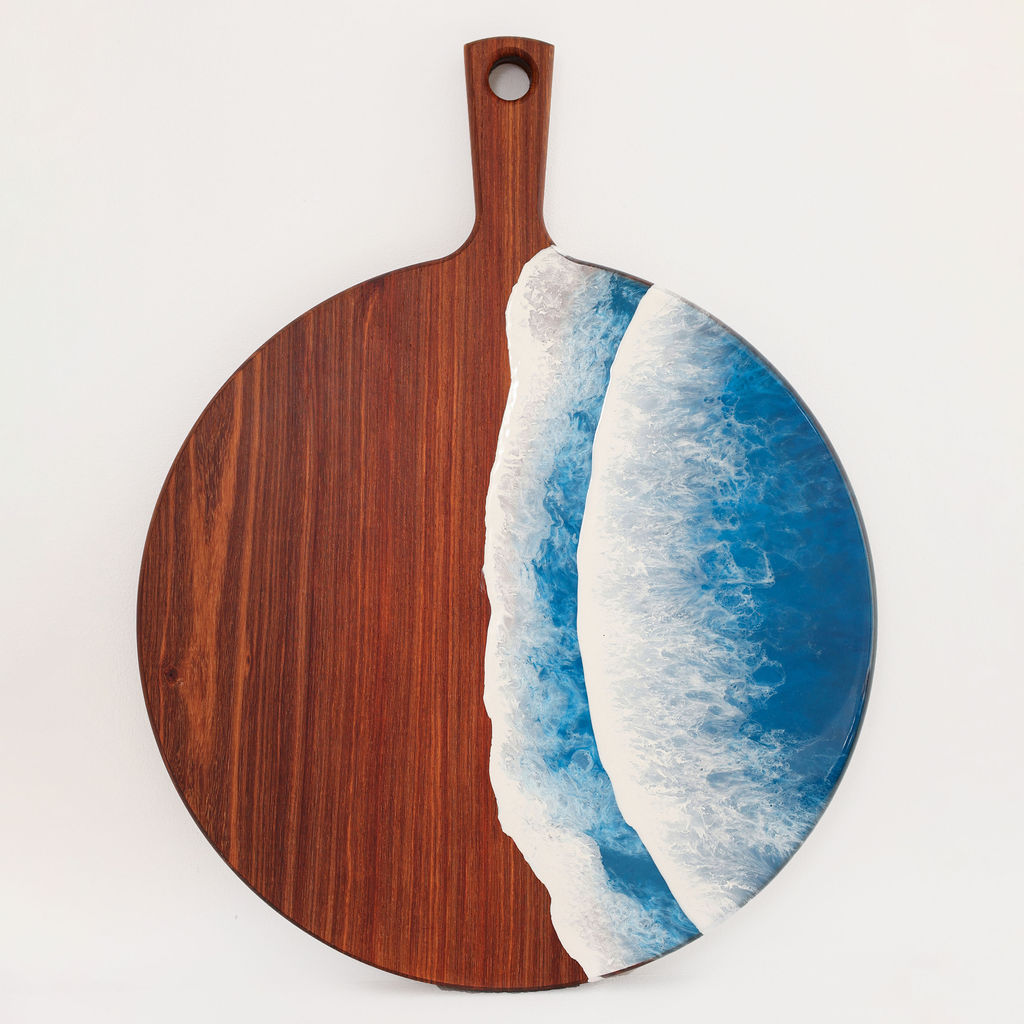 Front view of handcrafted round paddle kiaat wood serving board with blue ocean resin wave design