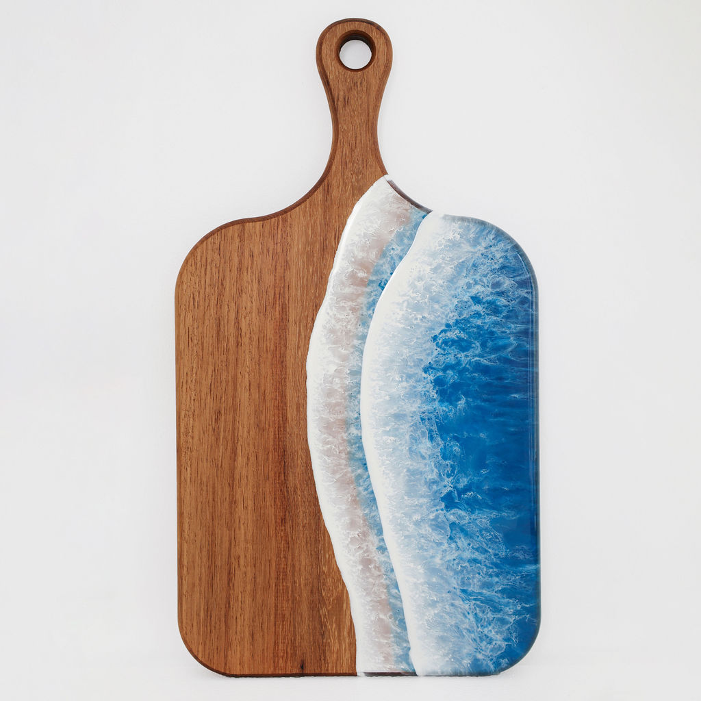 Front view of handcrafted medium paddle kiaat wood serving board with blue ocean resin wave design