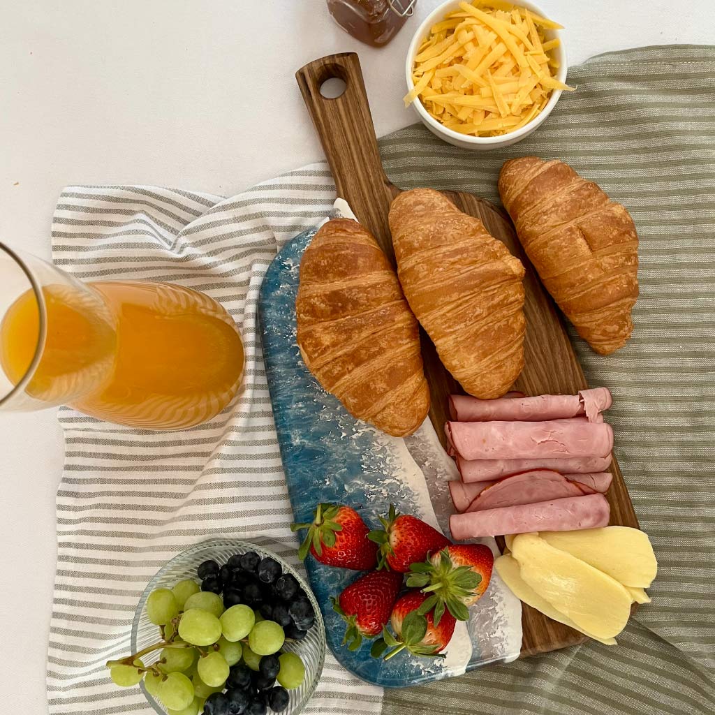 Handcrafted organic medium paddle serving board with ocean resin wave design styled with a variety of foods for entertaining